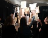 Osoby przeglądające zawieszone kartki z informacjami w mroku.