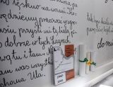 Ręcznie pisane notatki na ścianie, obok zrolowane dokumenty.
