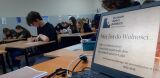 Uczniowie piszą prace w klasie, komputer z napisem na pierwszym planie.