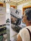 Starsza kobieta ogląda planszę „My mosinianie – przeszłość i teraźniejszość” na tle sali wystawowej.