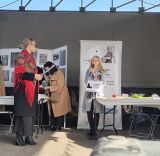 Kobieta przemawiająca do mikrofonu na tle roll-upu muzeum i tablic edukacyjnych.