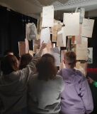 Grupa osób interakcjonuje z wiszącymi dokumentami w ciemnym pomieszczeniu.