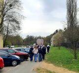 Grupa młodzieży idzie chodnikiem wzdłuż parkingu w stronę dużego pomnika w kształcie pękniętego serca.