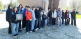 Grupa młodzieży pozuje z opiekunką przy pomniku w słoneczny dzień. Jedna osoba trzyma stare zdjęcie.