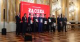 Grupa laureatów i gości honorowych pozująca do zdjęcia na scenie z dyplomami w dłoniach.