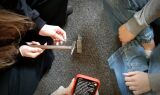 Widok z góry na dłonie dziewczyny trzymającej mały młotek nad miniaturowym kowadełkiem oraz ekran telefonu z tekstem.
