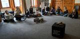 Młodzież siedząca w dużym półkolu na podłodze podczas zajęć edukacyjnych z pufą oznaczoną logo 'Muzeum Dzieci Polskich'.