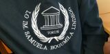 Zbliżenie na wyszywane, białe logo szkoły na ciemnej bluzie z napisem 'LO im. Samuela Bogumiła Lindego Toruń'.