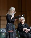 Kobieta mówi do mikrofonu, starsza kobieta słucha z zainteresowaniem.