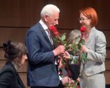 Osoba wręcza czerwoną różę mężczyźnie na scenie.