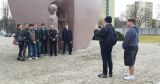 Grupa uczniów stoi przy Pomniku Pękniętego Serca w Łodzi; jeden z nich robi zdjęcie pozostałym na tle monumentu.