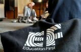 Zbliżenie na czarną torbę z logo 'Education First' na tle rozmytej sali warsztatowej.