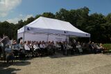 Seniorzy i zaproszeni goście siedzą pod białym namiotem podczas plenerowej uroczystości.