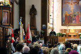 Wnętrze kościoła podczas mszy; obecni ludzie skierowani w stronę ołtarza, na którym stoi biskup, obok sztandary.