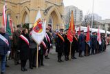 Poczet sztandarowy i mundurowi z flagami podczas uroczystości przed kościołem.