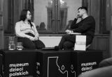 Czarno-białe ujęcie autorki i prowadzącego rozmawiających podczas spotkania w Muzeum. 
