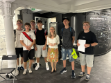 Grupa uczniów pozująca z panią przewodnik do zdjęcia w sali Muzeum.