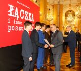Moment wręczania dyplomu i uścisk dłoni przedstawiciela instytucji z nagrodzonym uczniem.