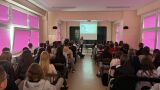 Sala z uczniami patrzącymi na prelegentkę stojącą na końcu sali pod ekranem projekcyjnym.