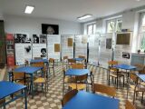 Sala z niebieskimi stolikami i wystawą zdjęć oraz tekstów.