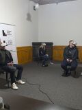 Trzy osoby siedzą na krzesłach w jasnym pomieszczeniu muzealnym, każda ma na głowie gogle VR i trzyma kontroler; na ścianie widoczny roll-up Muzeum Dzieci Polskich
