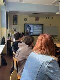 Uczniowie w ławkach szkolnych tyłem do obiektywu, patrzący na ekran prezentujący biografię dziewczynki o imieniu Gertruda Weinhold.