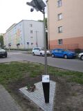 Lampa solarna przy ulicy, z monitoringiem i tablicą informacyjną.