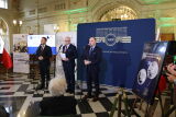 Konferencja prasowa w NBP, mężczyźni przy mikrofonach, dekoracje.