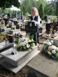 Kobieta przy grobie, otoczona kwiatami i zniczami.