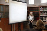 Kobieta prowadzi prezentację w bibliotece. Uczestnicy słuchają.