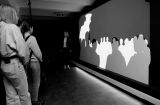 Ludzie obserwują projekcję w monochromatycznym otoczeniu.